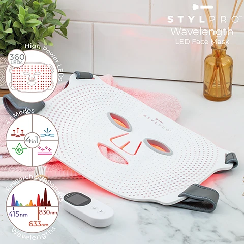 Image 1 - A white STYLPRO Wavelength LED Face Mask with visible red light rests on a pink towel in a bathroom setting with white tiles, a green plant, and a brown diffuser bottle, while surrounding infographics detail its features including 360 LEDs, High Power LEDs, 4x Modes, 4in1, Research Supported Wavelengths, 415nm, 830nm, and 633nm, with a STYLPRO remote control also present. Image 2 - A white light therapy mask with grey straps is shown, illuminated with red, blue, pink, and light pink lights, with four surrounding labels and text descriptions: Anti-ageing 633nm & 830nm Red light & NIF Helps promote Anti-ageing, Target 415nm Blue Light Setting, Balance A combined Balance of all wavelengths with the highest light, and Recovery 830nm Near Infrared Recovering overall skin health.